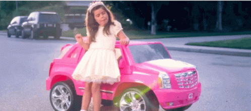 A Little Girl In A White Dress Sits In A Pink Toy Car GIF