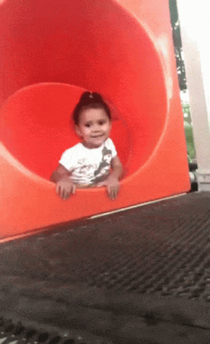 A Little Girl In A White Shirt Is Sitting On A Red Slide GIF
