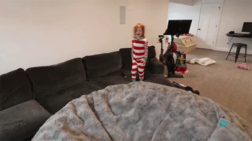 A Little Girl In Striped Pajamas Stands On A Couch GIF