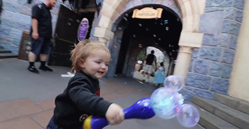 A Little Girl Is Blowing Soap Bubbles In Front Of A Building That Says Castle GIF