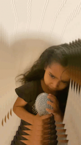 A Little Girl Is Brushing Her Hair In Front Of A Mirror GIF
