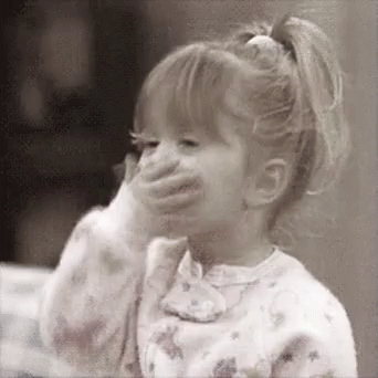 A Little Girl Is Covering Her Mouth With Her Hand And Smiling . GIF
