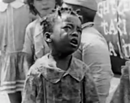 a little girl is crying in a black and white photo while standing in front of a sign .