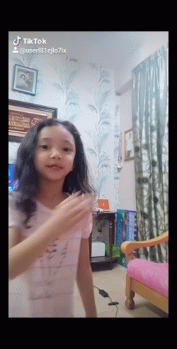 A Little Girl Is Dancing In A Room With A Pink Chair And A Picture On The Wall That Says Tiktok GIF