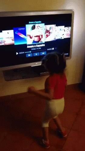A Little Girl Is Dancing In Front Of A Tv Screen That Says Amore Capoeira GIF