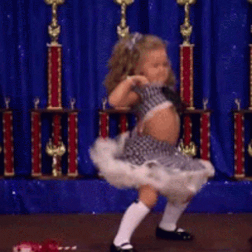 A Little Girl Is Dancing In Front Of Trophies And A Blue Curtain GIF