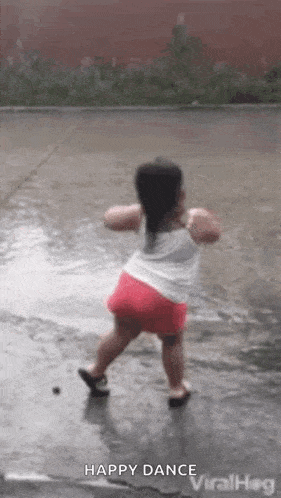 A Little Girl Is Dancing In The Rain In A Puddle Of Water . GIF