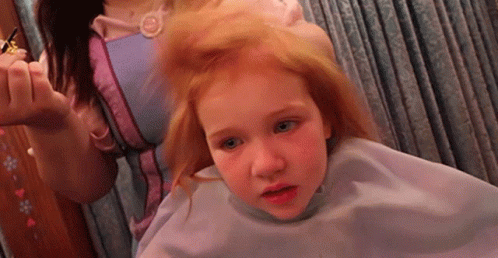 A Little Girl Is Getting Her Hair Cut By A Woman In A Pink Dress GIF