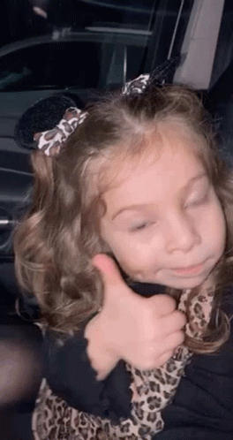 A Little Girl Is Giving A Thumbs Up While Sitting In A Car . GIF
