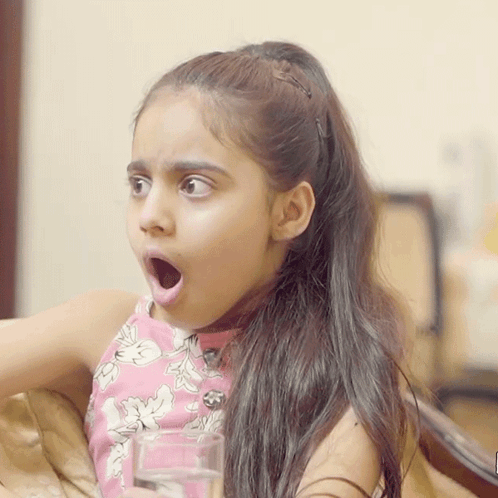 A Little Girl Is Holding A Glass Of Water With Her Mouth Open GIF