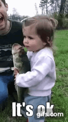 A Little Girl Is Holding A Large Fish In Her Arms . GIF