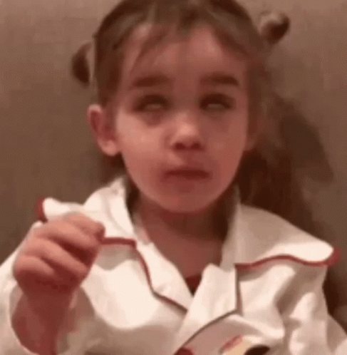 A Little Girl Is Holding A Piece Of Paper In Her Hand And Making A Face . GIF