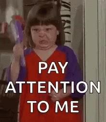 A Little Girl Is Holding A Toy And Making A Funny Face And Says `` Pay Attention To Me '' . GIF