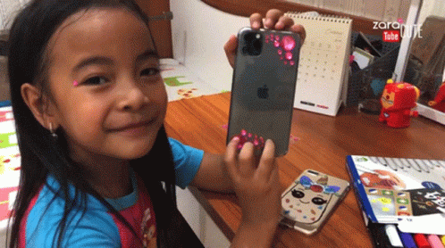 A Little Girl Is Holding An Apple Iphone In Her Hand GIF