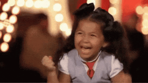 A Little Girl Is Laughing With Her Fist In The Air While Wearing A Vest And Tie . GIF