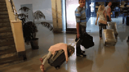 A Little Girl Is Laying On A Suitcase While A Man Pushes A Suitcase GIF