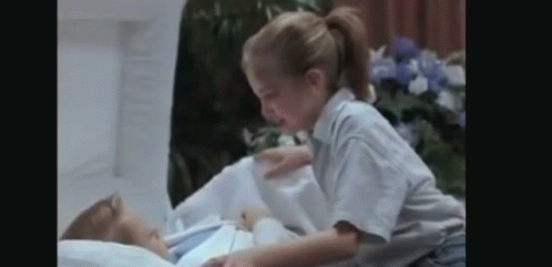 A Little Girl Is Laying On Top Of A Corpse In A Hospital Bed . GIF