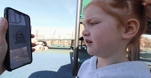 A Little Girl Is Looking At A Phone With A Ghost On The Screen GIF