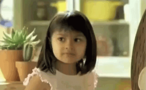 A Little Girl Is Making A Funny Face While Sitting At A Table With Potted Plants . GIF