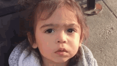 A Little Girl Is Making A Funny Face While Standing On The Sidewalk . GIF