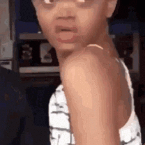 A Little Girl Is Making A Funny Face While Wearing A White Tank Top . GIF