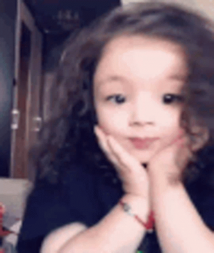 A Little Girl Is Making A Funny Face With Her Hands On Her Face . GIF