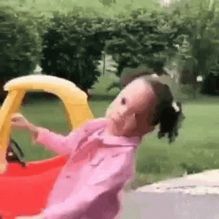 A Little Girl Is Riding In A Toy Car . GIF