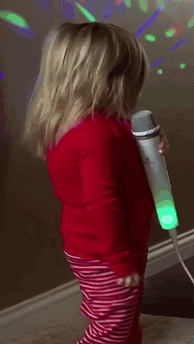 A Little Girl Is Singing Into A Microphone In A Room GIF