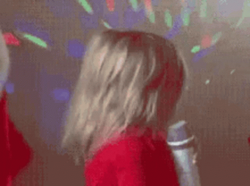 A Little Girl Is Singing Into A Microphone While Wearing A Red Sweater . GIF