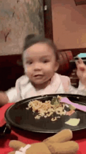 A Little Girl Is Sitting At A Table Eating A Plate Of Food . GIF