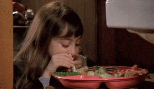 A Little Girl Is Sitting At A Table Eating A Plate Of Food With A Fork . GIF