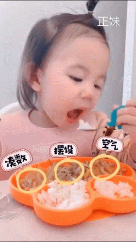 A Little Girl Is Sitting At A Table Eating Food From A Flower Shaped Plate GIF