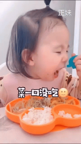 A Little Girl Is Sitting At A Table Eating Food From An Orange Plate With A Smiley Face On It . GIF