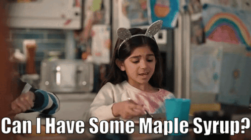a little girl is sitting at a table with a cup of maple syrup