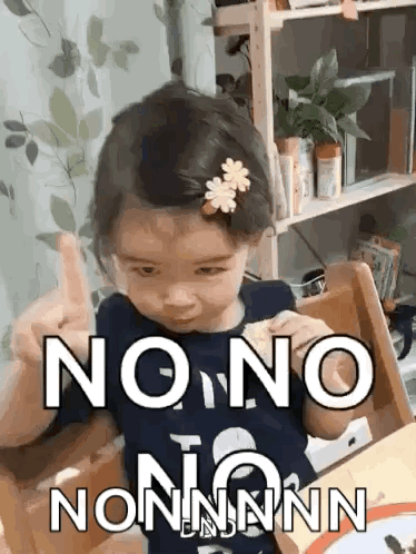A Little Girl Is Sitting At A Table With A Flower In Her Hair Giving The Middle Finger . GIF