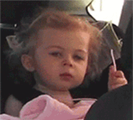 A Little Girl Is Sitting In A Car Seat Holding A Lollipop GIF
