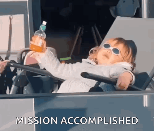 A Little Girl Is Sitting In A Chair Holding A Bottle Of Orange Juice And The Words Mission Accomplished Behind Her GIF
