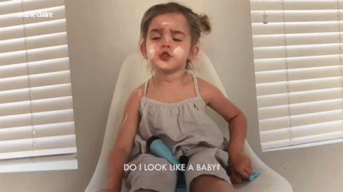 A Little Girl Is Sitting In A Chair With Her Eyes Closed And The Words Do I Look Like A Baby Above Her GIF
