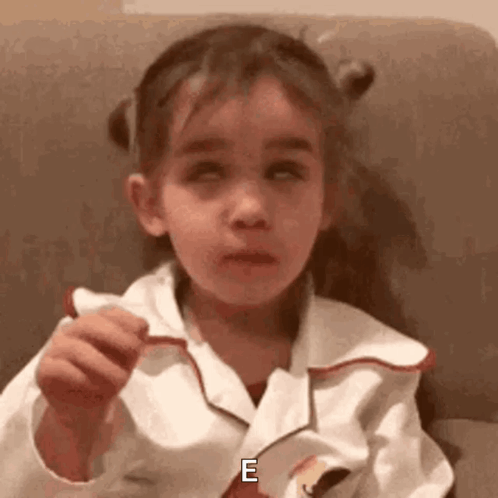 A Little Girl Is Sitting On A Couch Holding A Piece Of Paper And Making A Funny Face . GIF