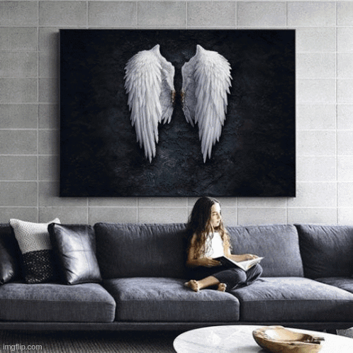 A Little Girl Is Sitting On A Couch Reading A Book Under A Painting Of Angel Wings GIF