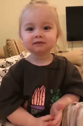 A Little Girl Is Sitting On A Couch Wearing A T-Shirt With A Cactus On It . GIF