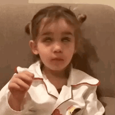 A Little Girl Is Sitting On A Couch With Her Eyes Closed And Eating A Cookie . GIF