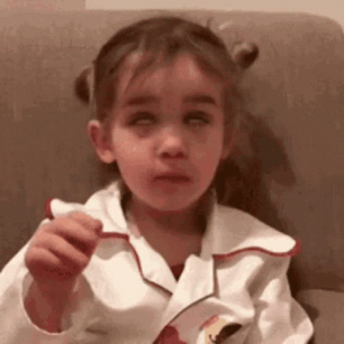 A Little Girl Is Sitting On A Couch With Her Eyes Closed And Eating A Cookie . GIF