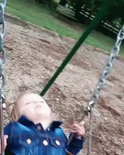 A Little Girl Is Sitting On A Swing In A Park With Her Eyes Closed . GIF