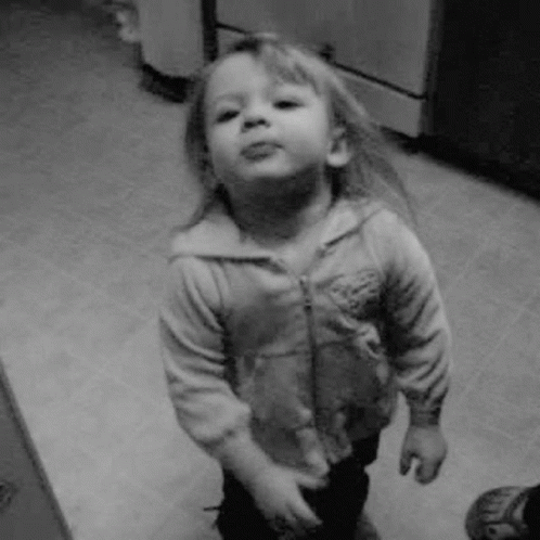 a little girl is standing in a kitchen and making a funny face in a black and white photo .