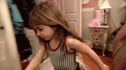 A Little Girl Is Standing In A Room With Her Hair In The Air . GIF