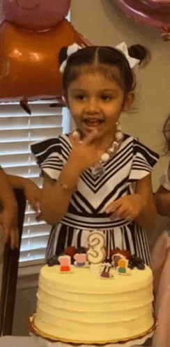 A Little Girl Is Standing In Front Of A Cake That Has The Number 3 On It GIF