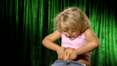 Girl Standing In Front Of Green Curtain Holding Stomach GIF