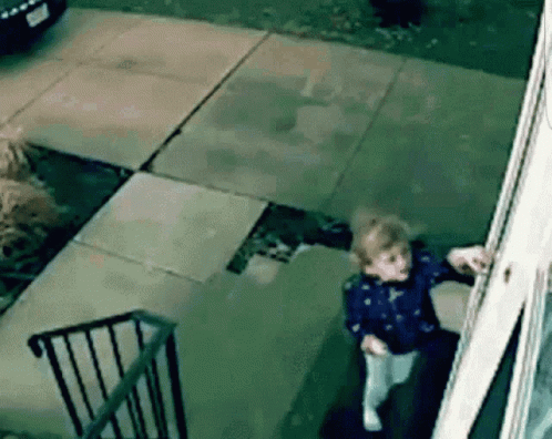 A Little Girl Is Standing In Front Of A House Looking Out A Window . GIF