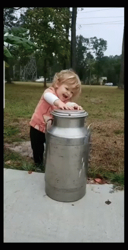 A Little Girl Is Standing Next To A Large Metal Can GIF
